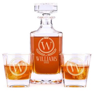 A personalized whiskey decanter set includes a square glass decanter and two matching glasses with an engraved \“WILLAMS 2022\“ and \“W\“ monogram.