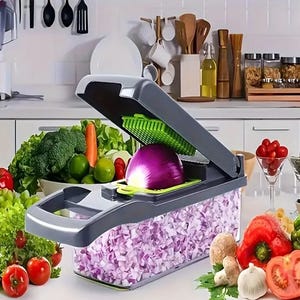 A vegetable chopper with a purple onion being chopped into diced pieces contained in its clear collection bin, surrounded by various fresh vegetables.