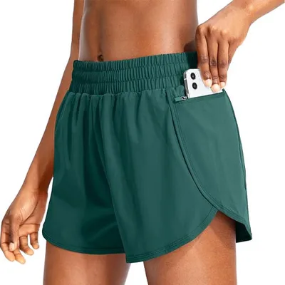 A person wears dark green athletic shorts with an elastic waistband, featuring a side zipper pocket where a smartphone is partially inserted.