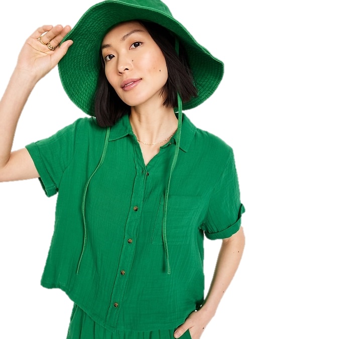 A woman is wearing a green short-sleeve shirt and matching wide-brimmed hat, accessorized with a small gold necklace and rings.