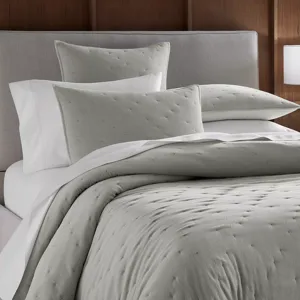 A neatly made bed with a light gray dotted duvet cover, matching pillows, and white sheets, set against a gray headboard and wooden wall backdrop.