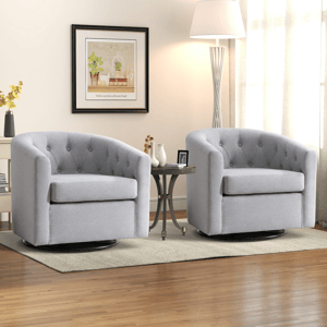 Two gray swivel armchairs with tufted backs are placed on a light rug, separated by a round side table with decorative items. A floor lamp and framed wall art complete the cozy living room setup.