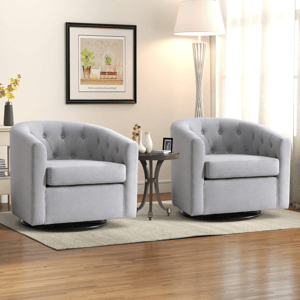 Two gray swivel armchairs with tufted backs are placed on a light rug, separated by a round side table with decorative items. A floor lamp and framed wall art complete the cozy living room setup.