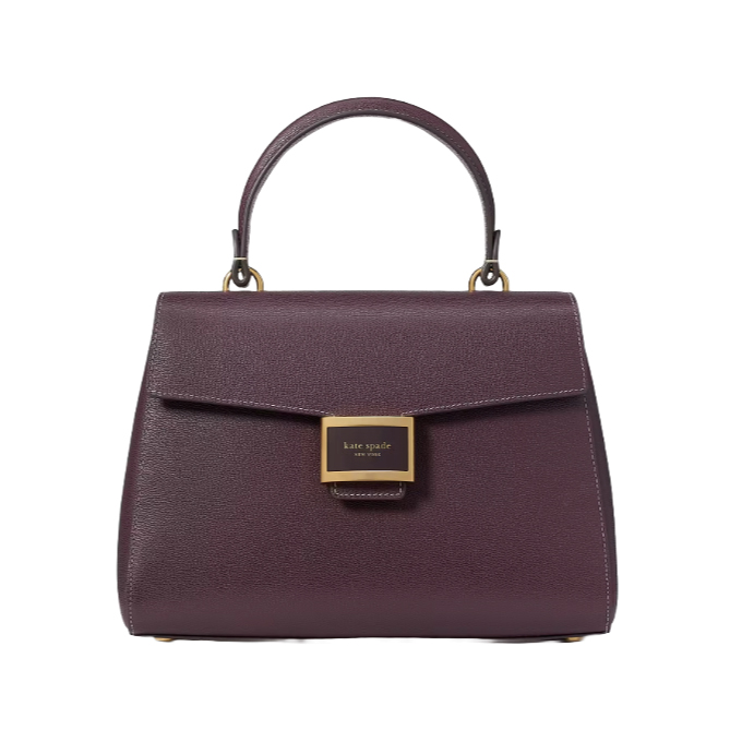 A maroon leather handbag with a structured design features a top handle and a front flap secured by a gold rectangular clasp labeled \“kate spade new york.\“