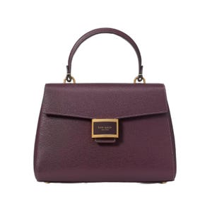A maroon leather handbag with a structured design features a top handle and a front flap secured by a gold rectangular clasp labeled \“kate spade new york.\“