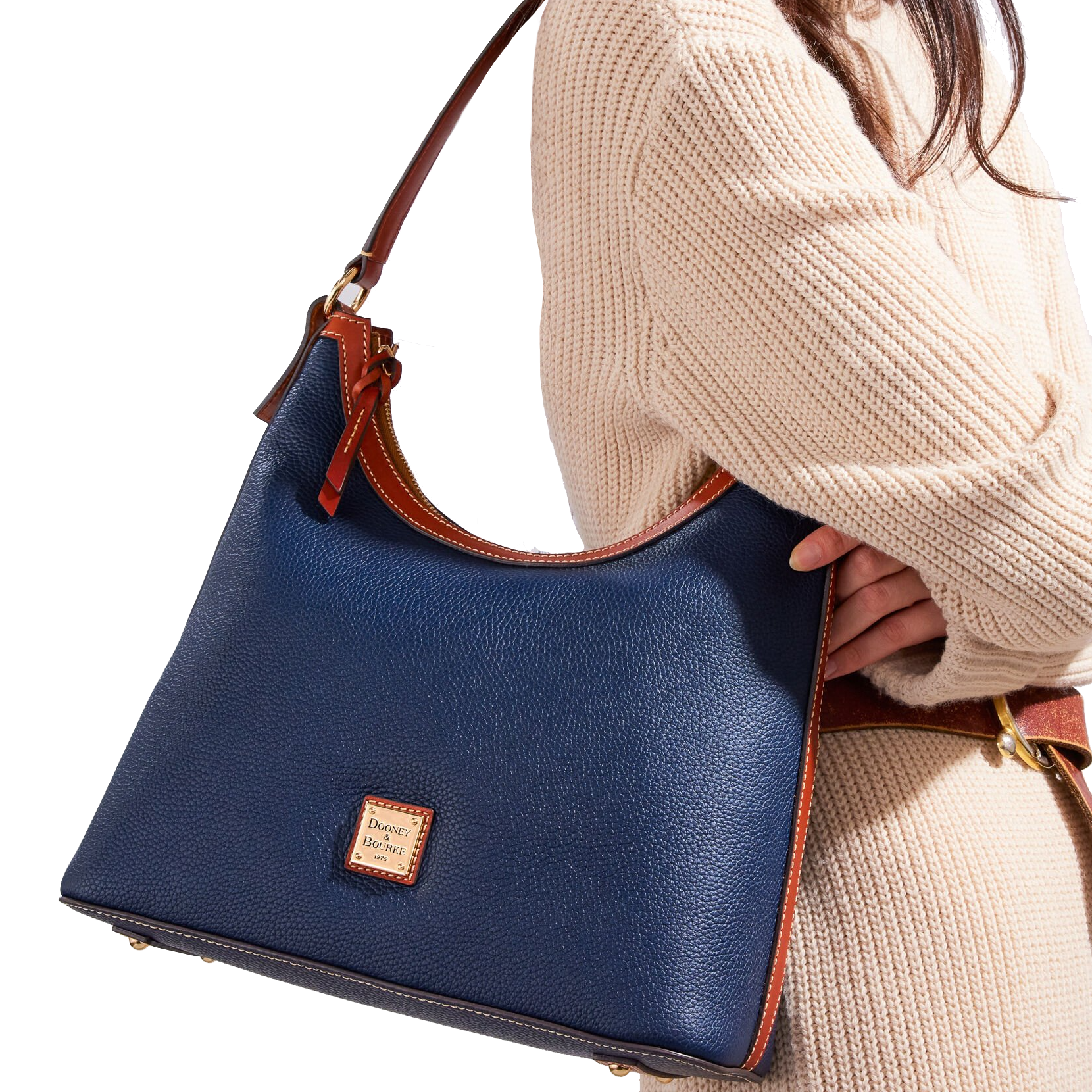 A navy Dooney & Bourke Pebble-Grain Leather Hobo with brown leather trim and a shoulder strap, featuring a label on the front. It's paired with a cream knit sweater.