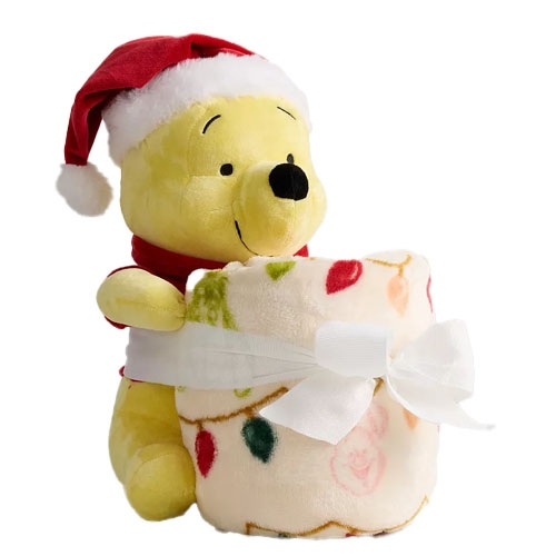 A plush toy wearing a Santa hat holds a rolled-up blanket with a festive lights pattern, tied with a white ribbon.