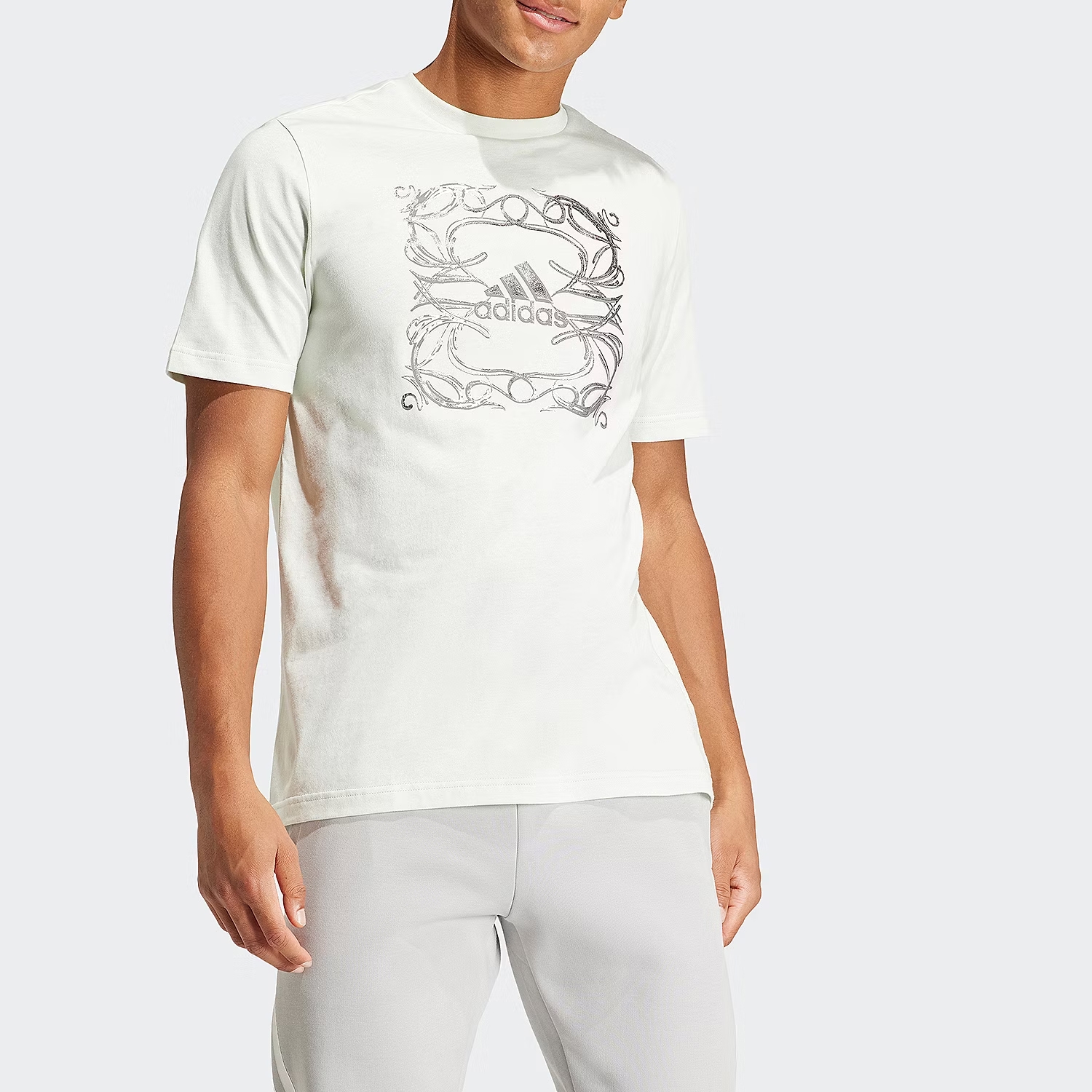 A man is wearing a white short-sleeved T-shirt with an ornate graphical print around the Adidas logo.