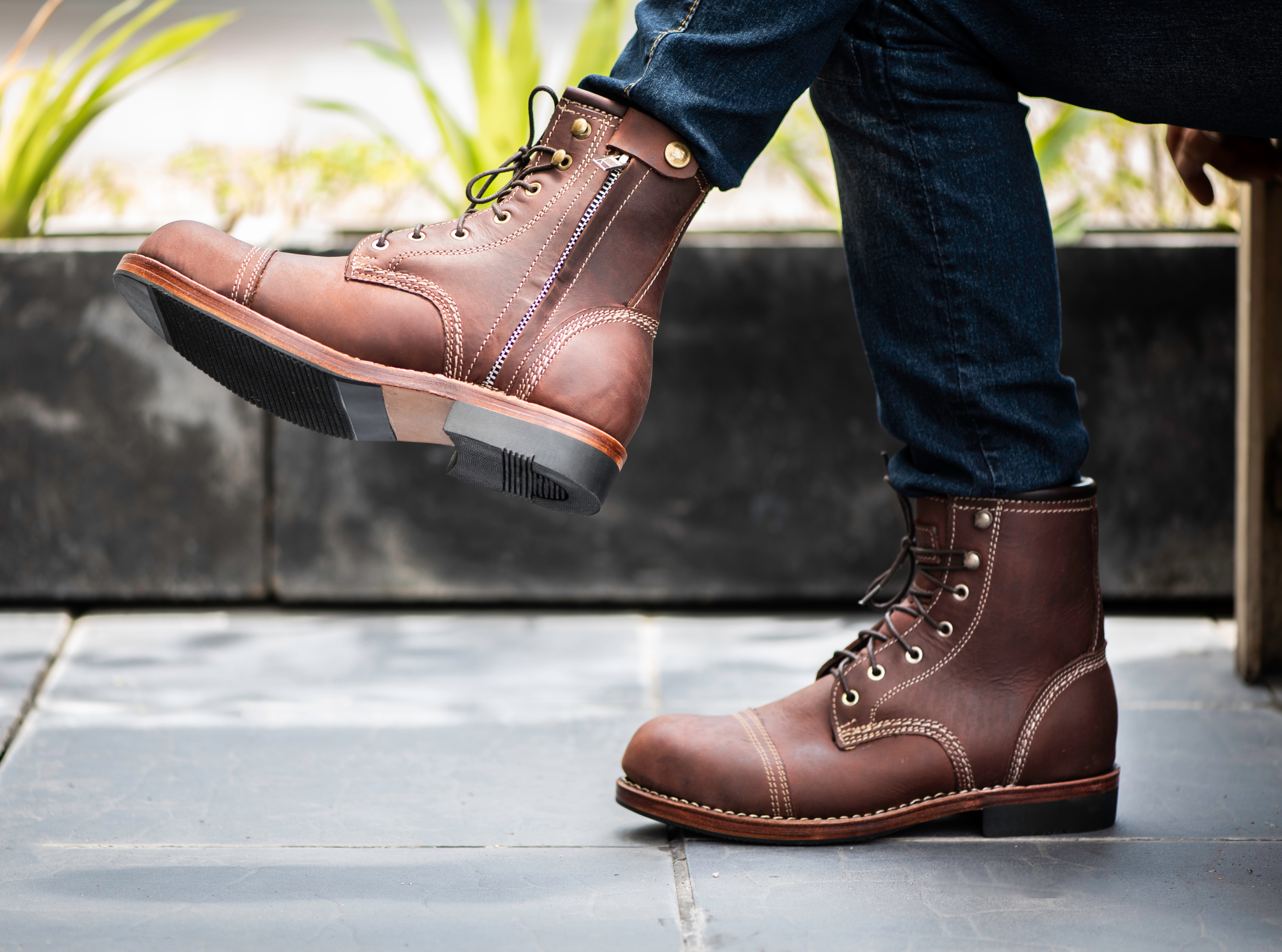 A person is wearing brown leather lace-up boots with prominent stitching details.