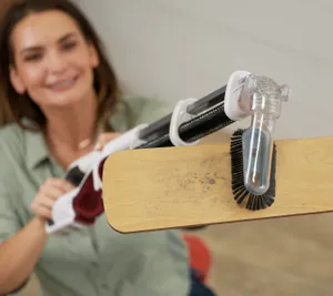 A person is happily showing a vacuum cleaner with a detachable handheld unit and a motorized brush head.