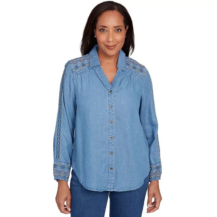 A woman wears a long-sleeve denim button-up shirt with colorful embroidery on the shoulders and sleeves, paired with matching blue jeans.