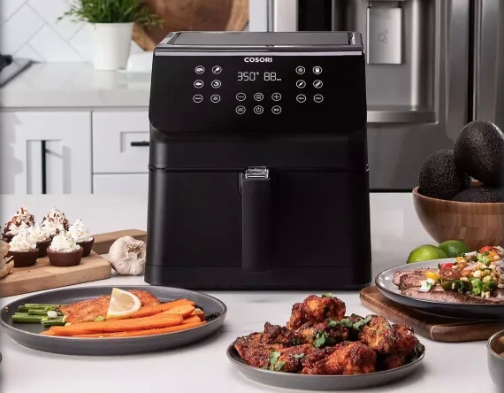 A black 5.8-quart Cosori air fryer with a digital control panel is displayed on a kitchen counter, surrounded by cooked food.