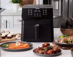 A black 5.8-quart Cosori air fryer with a digital control panel is displayed on a kitchen counter, surrounded by cooked food.