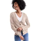 A woman is wearing a beige V-neck cardigan with brown buttons, over a white top, paired with blue jeans.