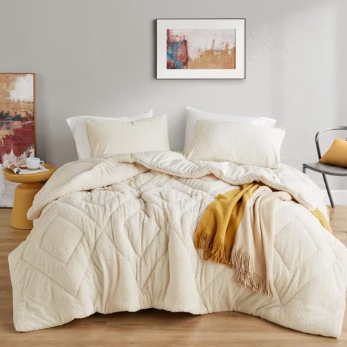 A king-sized comforter set in cream color with a diamond stitch pattern, accompanied by two matching pillow shams and a golden yellow throw blanket.