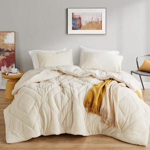 A king-sized comforter set in cream color with a diamond stitch pattern, accompanied by two matching pillow shams and a golden yellow throw blanket.