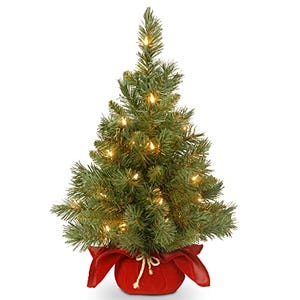 A small artificial Christmas tree with LED lights and a red cloth base, designed to be displayed on a tabletop.