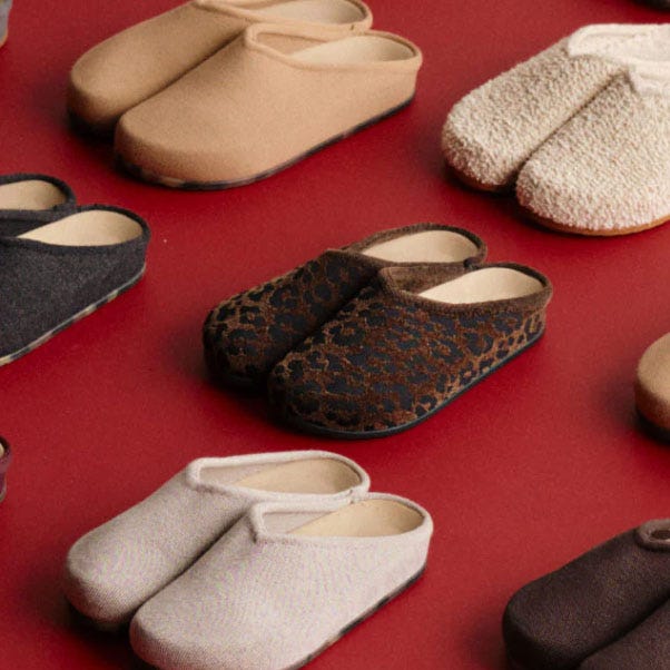 A variety of slip-on slippers in different colors and textures, including beige, black, leopard print, and cream, are displayed on a red surface.