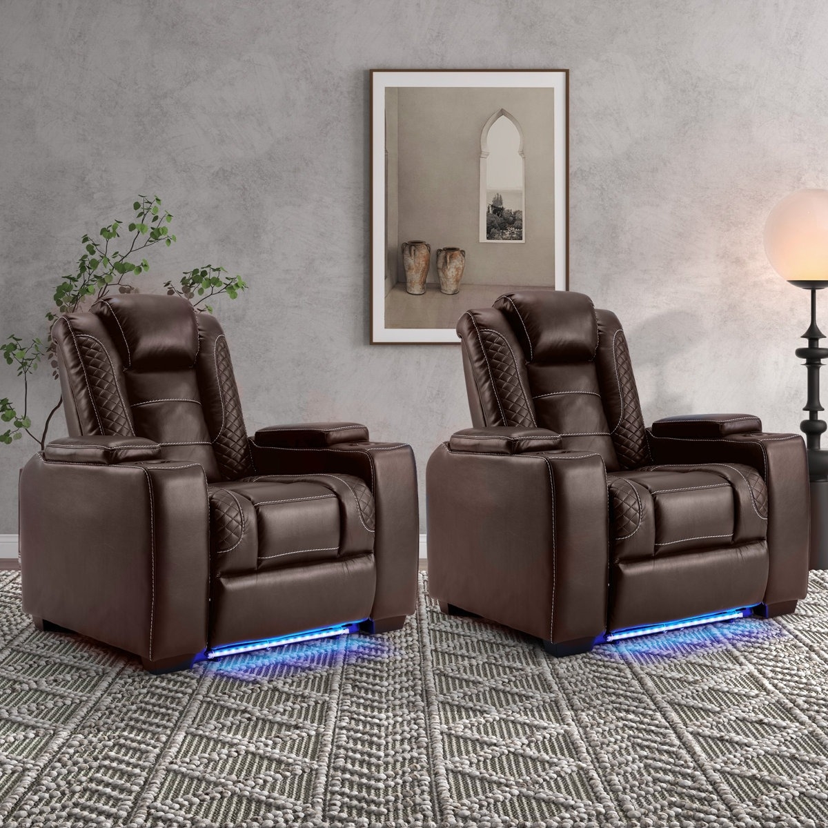 A pair of brown leather recliner chairs with blue LED lighting underneath, featuring quilted accents and cup holders, placed on a textured rug with a minimalist decorative setting.