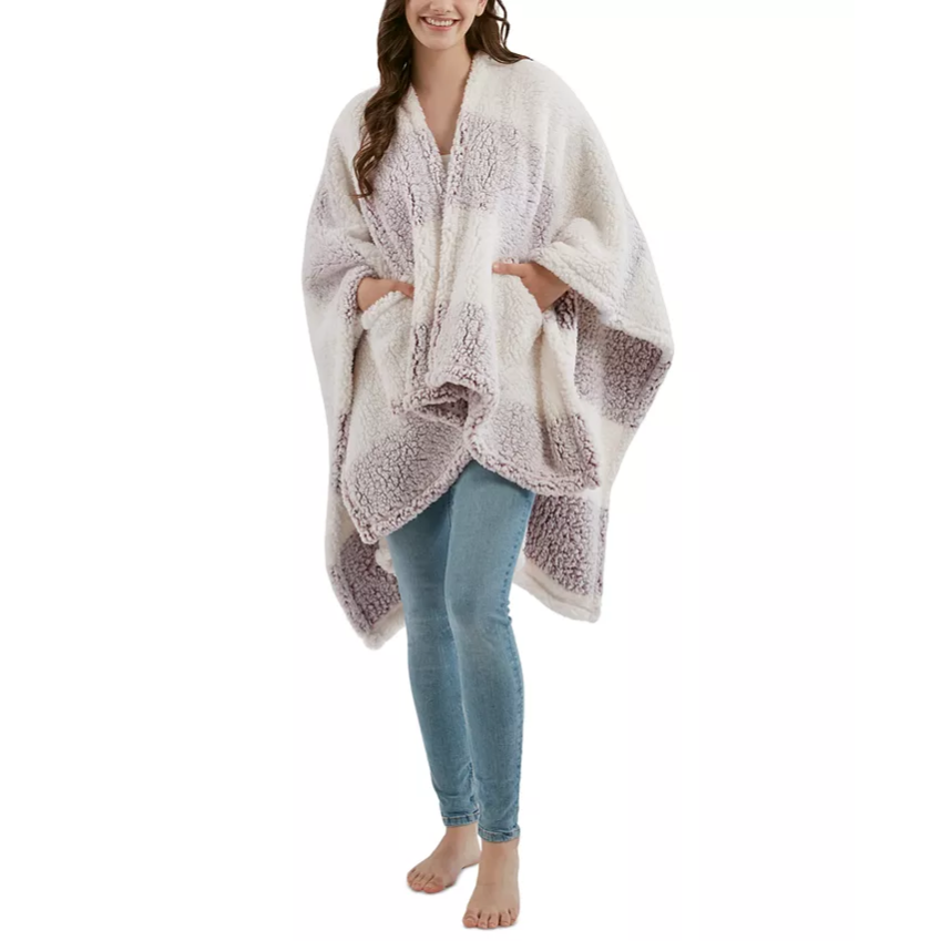 A woman is wearing a cozy, oversized sherpa plaid poncho in shades of white and light gray, paired with light blue skinny jeans.