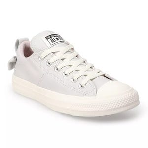 Converse Women's Chuck Taylor Sneaker features a classic low-top design with white canvas, rubber toe cap, and lace-up closure. It has a subtle bow detail on the heel and a logo patch on the tongue.