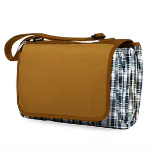 A compact picnic blanket tote with a plaid design on the sides and a brown flap cover, featuring an adjustable shoulder strap for easy carrying.
