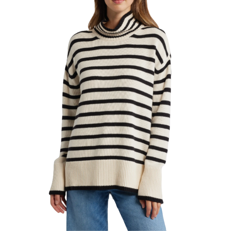 A woman is wearing a cream and black striped turtleneck sweater with long sleeves and ribbed cuffs, paired with blue jeans.