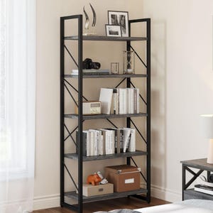 A 5-tier bookshelf features a black metal frame with wooden shelves, displaying books, framed photos, decorative items, and storage boxes. It stands near a window, adding a sleek, functional design to the room.