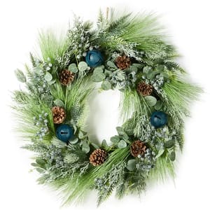 A lush wreath featuring green foliage, pine cones, blue berries, and large blue bells. The design combines various textures and shades of green for a festive look.
