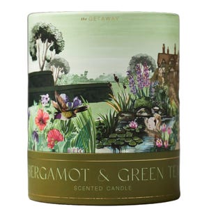 Scented candle labeled \“Bergamot & Green Tea\“ from \“The Getaway\“ series, featuring a decorative illustration of a garden scene with plants, flowers, a bird, and a pond.
