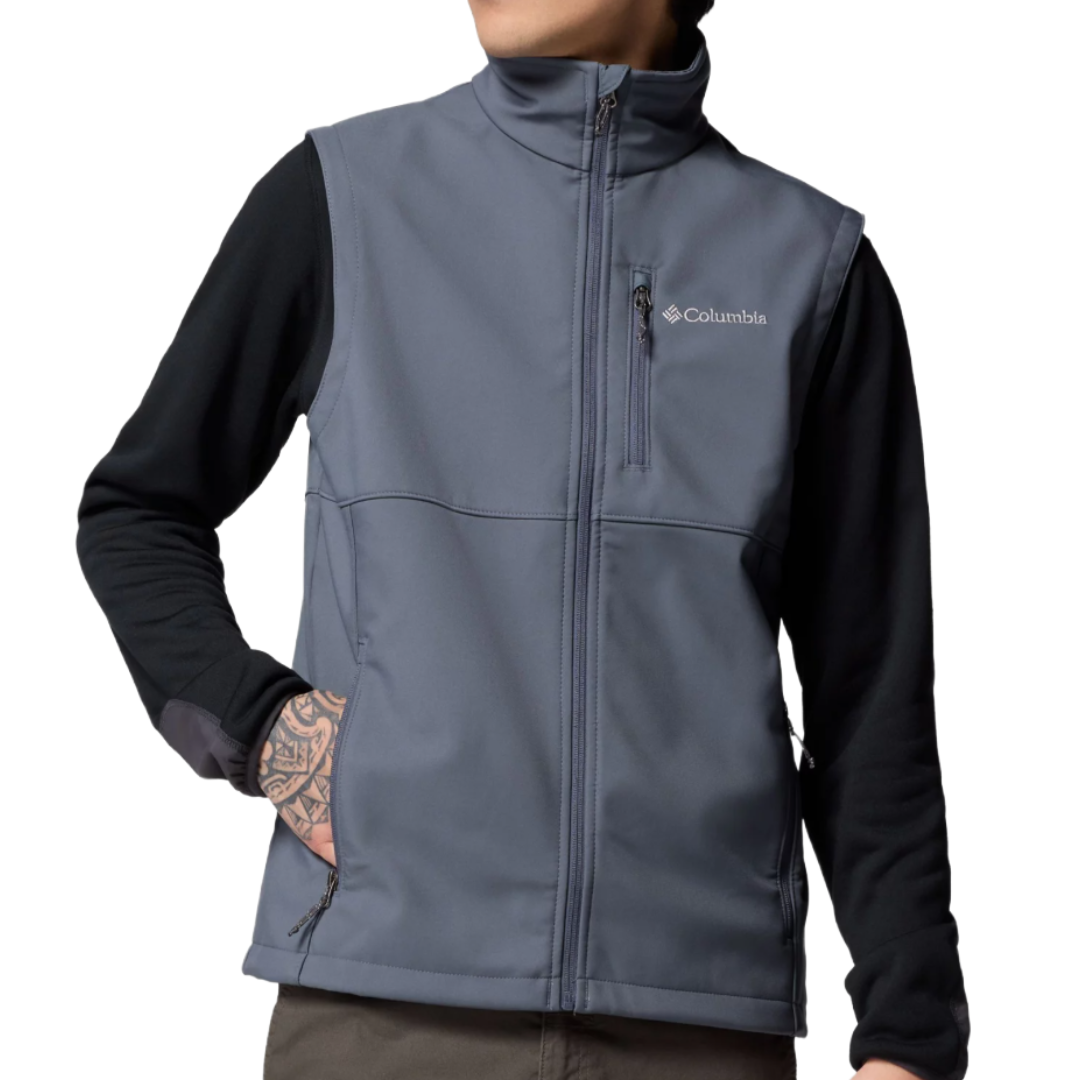 A man wearing a gray Columbia softshell vest over a black long-sleeve shirt, featuring a zippered chest pocket and hand pockets, with visible tattoos on the arm.