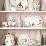 Festive dishware collection featuring characters from a popular holiday story, displayed with holiday-themed decorations like miniature trees and figurines.