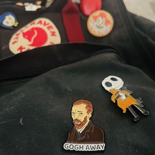 A dark-colored Fjallraven backpack with various enamel pins featuring Van Gogh and Jack Skellington.