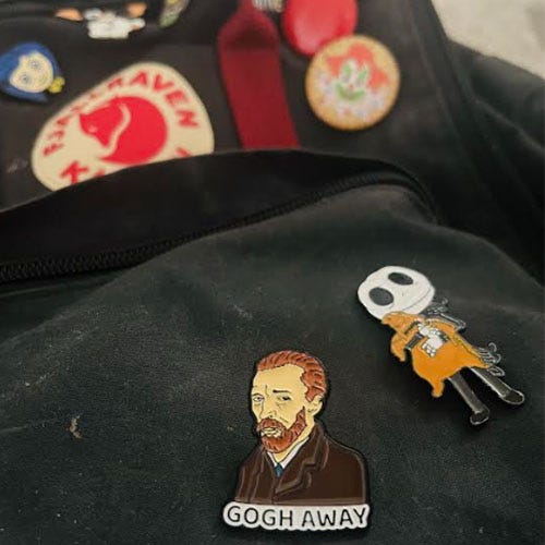 A dark-colored Fjallraven backpack with various enamel pins featuring Van Gogh and Jack Skellington.