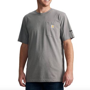 A person wearing a gray short-sleeve Carhartt T-shirt with a chest pocket and logo on the sleeve, paired with dark blue jeans.