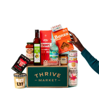 A variety of groceries from Thrive Market, including Banza pasta, scout snacks, Chomps, and Rao's sauce, displayed alongside Oatly, snacks, and other assorted items in a Thrive Market box.