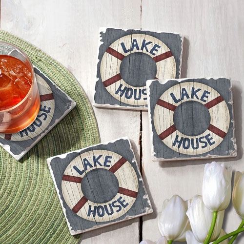 Square coasters with a \“Lake House\“ lifebuoy design, placed on a green placemat next to a drink and white tulips.