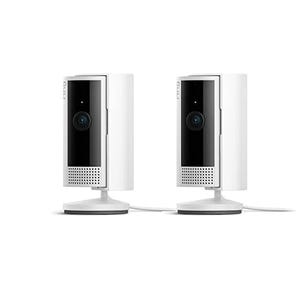 Two white Ring Indoor Cameras with black fronts, featuring a lens and speaker grill on each. They are mounted on small circular bases. These cameras are designed for indoor video monitoring.