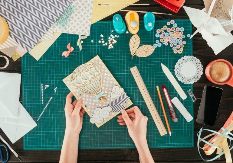 Crafting materials including patterned paper, a handmade card, punches, ribbons, and decorative embellishments on a work mat.