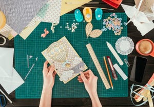 Crafting materials including patterned paper, a handmade card, punches, ribbons, and decorative embellishments on a work mat.