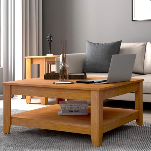 A wooden coffee table with a lower shelf, housing a laptop, decorative items, and books.