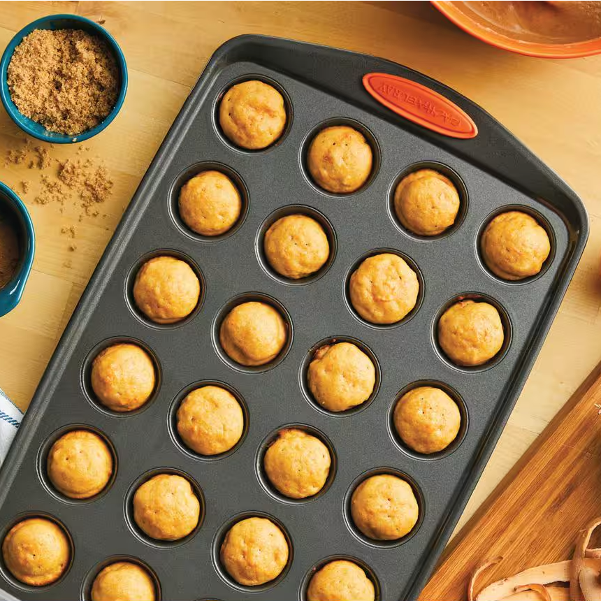 A pan with 12 freshly baked mini muffins sits next to a bowl of brown sugar.