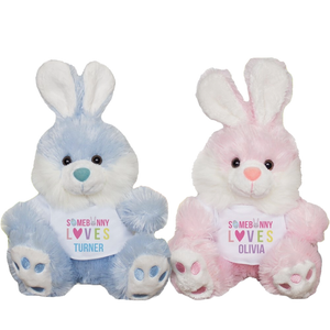 Two plush Easter bunny toys, one blue and one pink, featuring personalized bibs that say \“Somebunny Loves Turner\“ and \“Somebunny Loves Olivia.\“ They have floppy ears and embroidered paw details.
