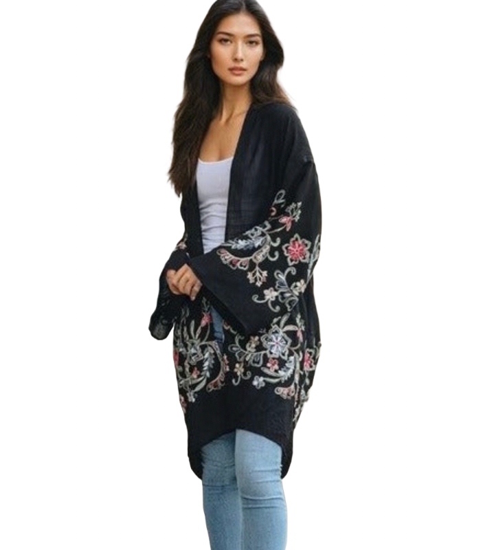 A woman wearing a black floral kimono cardigan over a white tank top paired with light blue jeans.