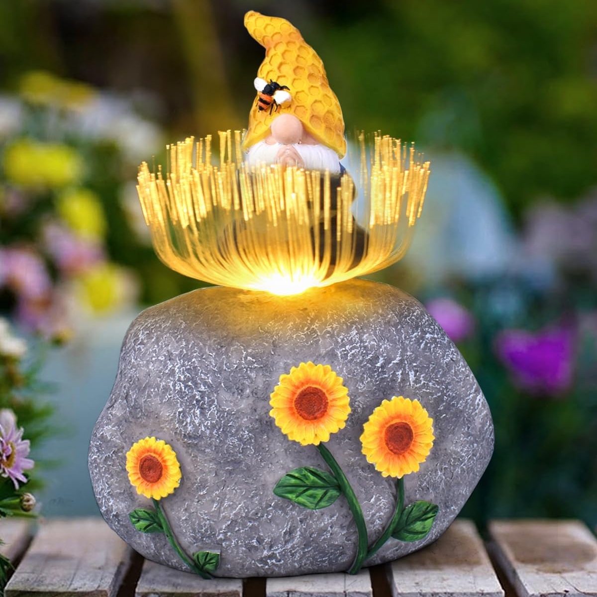 A garden ornament featuring a gnome with a honeycomb hat and bee, sitting on a stone with glowing fiber optic strands emerging, decorated with three sunflowers.