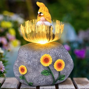A garden ornament featuring a gnome with a honeycomb hat and bee, sitting on a stone with glowing fiber optic strands emerging, decorated with three sunflowers.