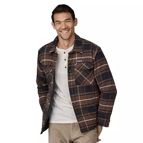 A man is wearing a Patagonia insulated flannel shirt with a brown and navy plaid pattern. The shirt features a button-up front, two chest pockets, and is layered over a light-colored henley shirt.