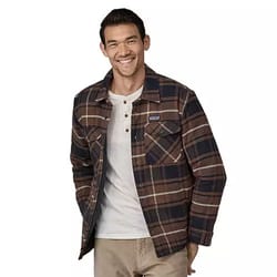 A man is wearing a Patagonia insulated flannel shirt with a brown and navy plaid pattern. The shirt features a button-up front, two chest pockets, and is layered over a light-colored henley shirt.