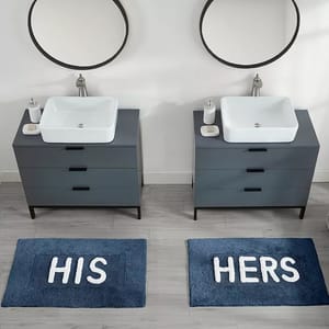 Double bathroom vanity set featuring two circular mirrors, white rectangular sinks, and gray cabinets, with blue rugs labeled \“His\“ and \“Hers\“ placed on a light gray floor.