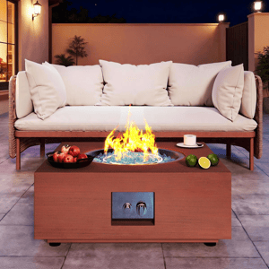 A patio with a modern fire pit table featuring a flame surrounded by blue glass, accompanied by a cup and limes. Nearby, a cushioned outdoor sofa and a bowl of apples sit on paved flooring.